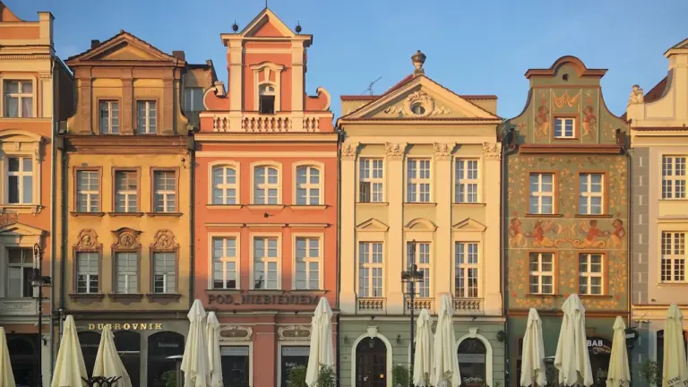 Historyczny rynek w Poznaniu z kamienicami i parasolami w letni słoneczny dzień.
