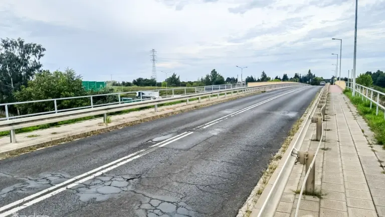 Asfaltowy most z widocznymi spękaniami nawierzchni, barierkami ochronnymi oraz chodnikiem w pochmurny dzień.