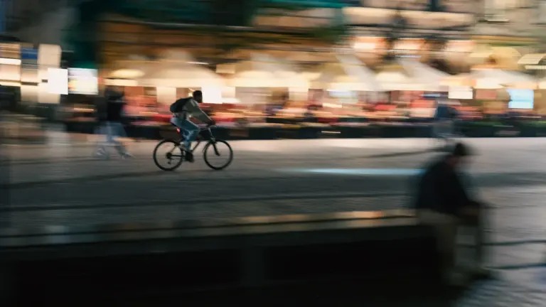 Rowerzysta jadący nocą przez miasto z efektem rozmycia ruchu w oświetlonym otoczeniu.