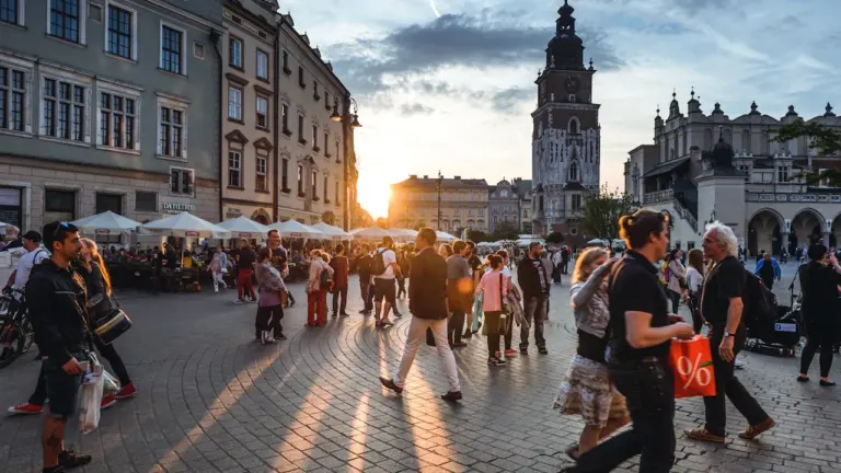 Turyści spacerujący po Rynku Głównym w Krakowie w promieniach zachodzącego słońca.