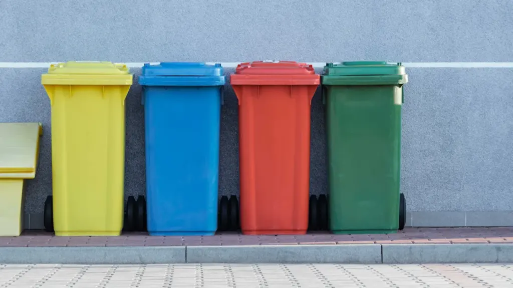 Rząd kolorowych pojemników na odpady segregowane przy szarej ścianie budynku w mieście.
